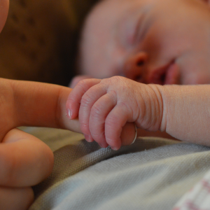 A newborn baby holding a person's finger