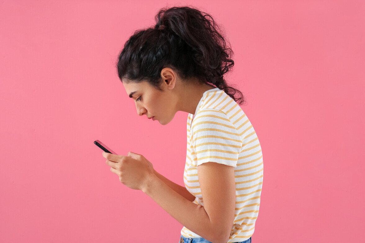 A woman standing hunched over while on her phone