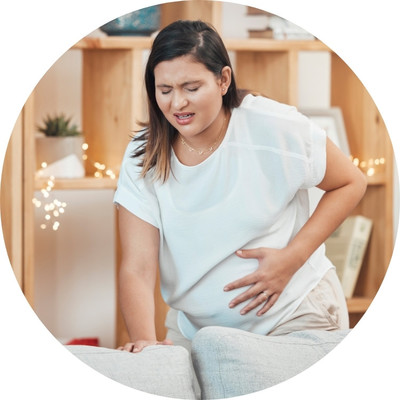 A pregnant woman with brown hair wearing a white shirtholding her stomach.