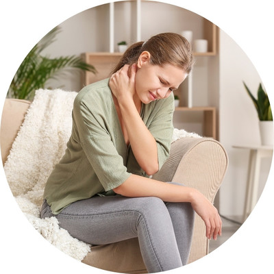 A woman sitting on a couch wearing a green shirt holding her sore neck.